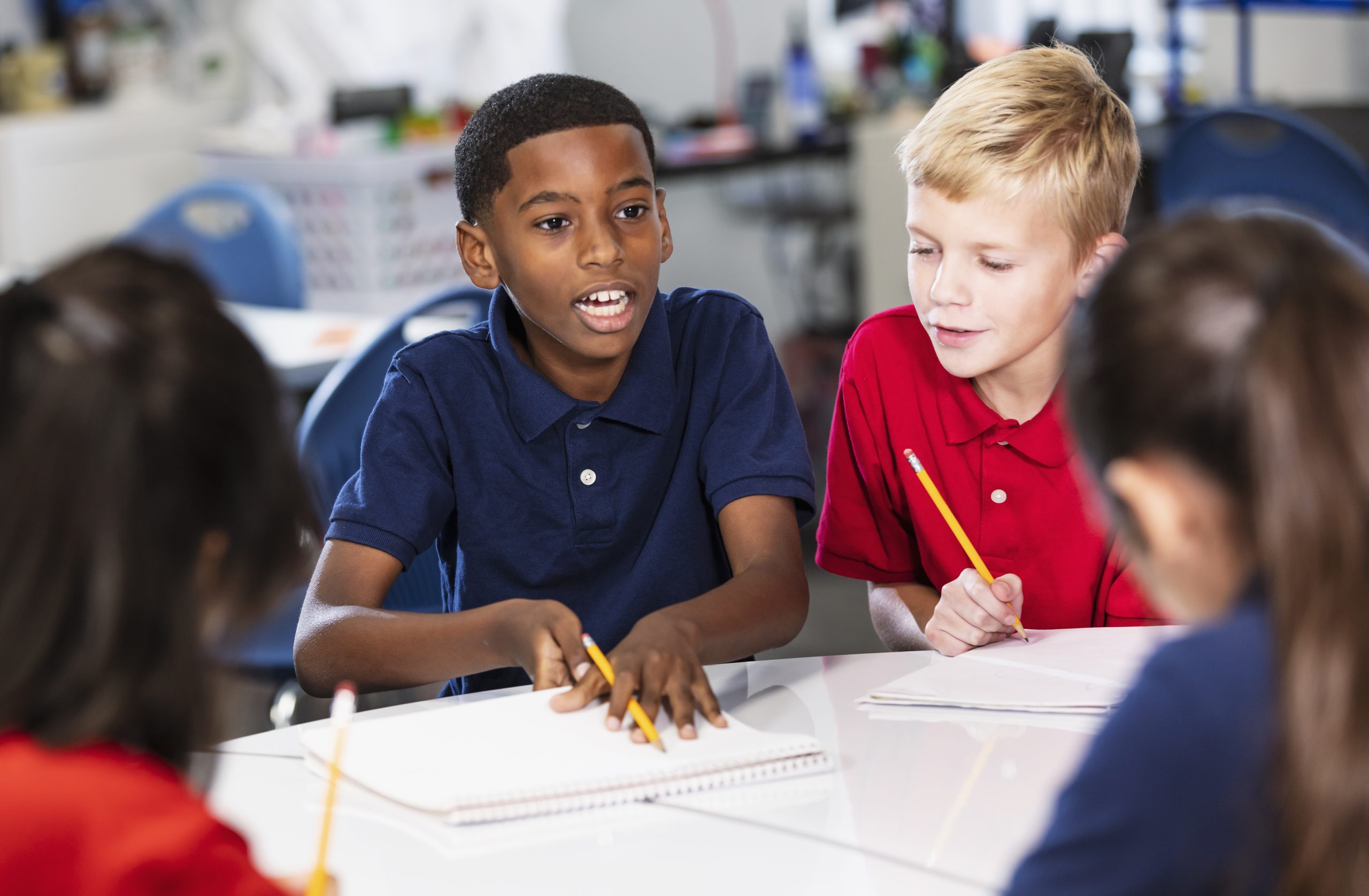 Middle school students in class doing writing assignment Headshot of two multiracial boys in their middle school classroom, sitting at a table doing a writing assignment. The African-American boy is looking up, talking, perhaps asking a question.